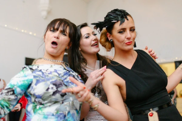 A young couple dances together at the wedding reception, the woman laughing with her eyes closed as the man makes a comical expression. Candid documentary wedding moment.