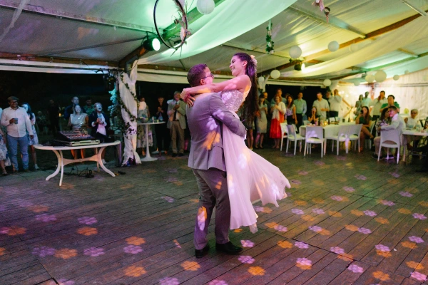 Newlyweds dancing under tent with dynamic purple and green uplighting at wedding reception.