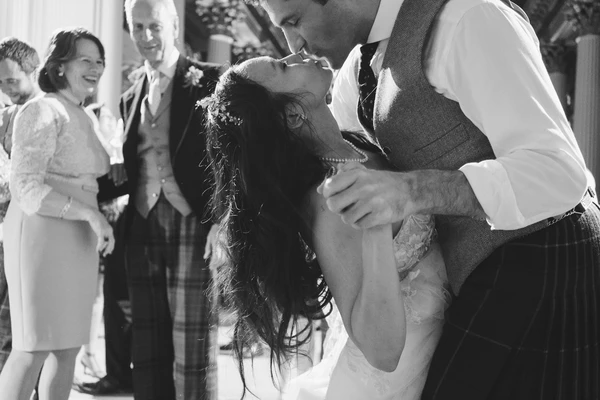 Groom gently lifts the bride's veil before the first kiss — guests watching with smiles