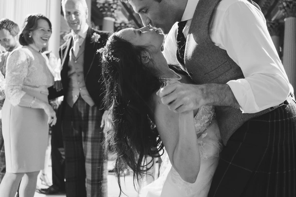Groom gently lifts the bride's veil before the first kiss — guests watching with smiles