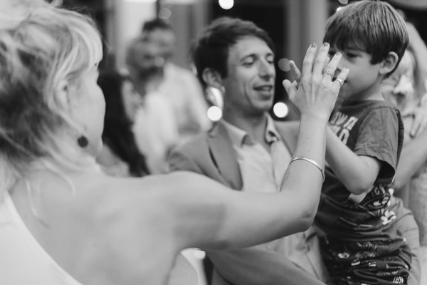 Young boy raises his hand toward the bride mid-dance — black-and-white, joyful wedding guests