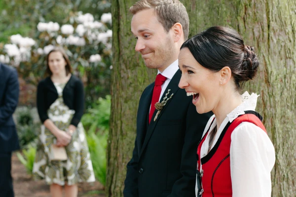 Bride bursting into joyful laughter beside the groom during the outdoor ceremony, guests watching with delight in the background. Candid emotional ceremony moment.