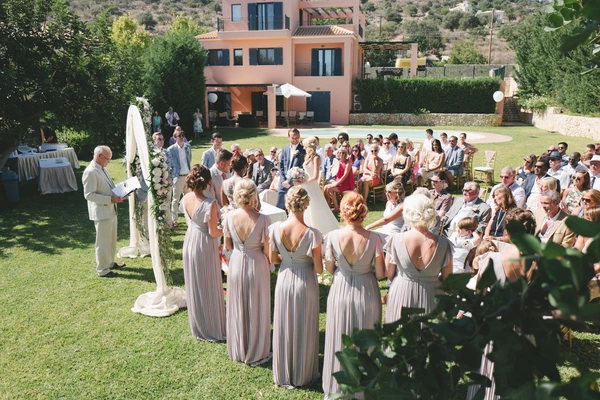 Outdoor ceremony — bride and witnesses facing guests, groom and officiant behind, terracotta house