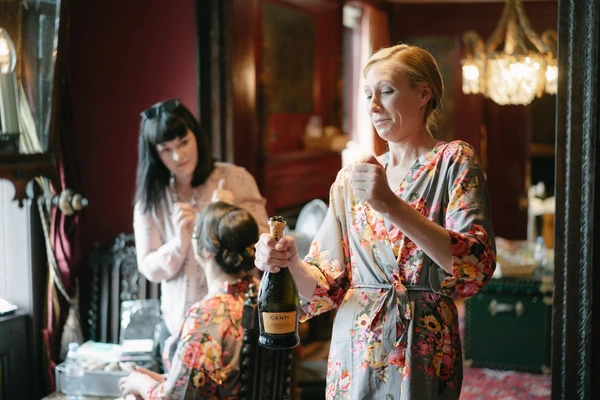 Three women in floral kimonos in a red salon, one holding champagne and Canti bottle, smiling