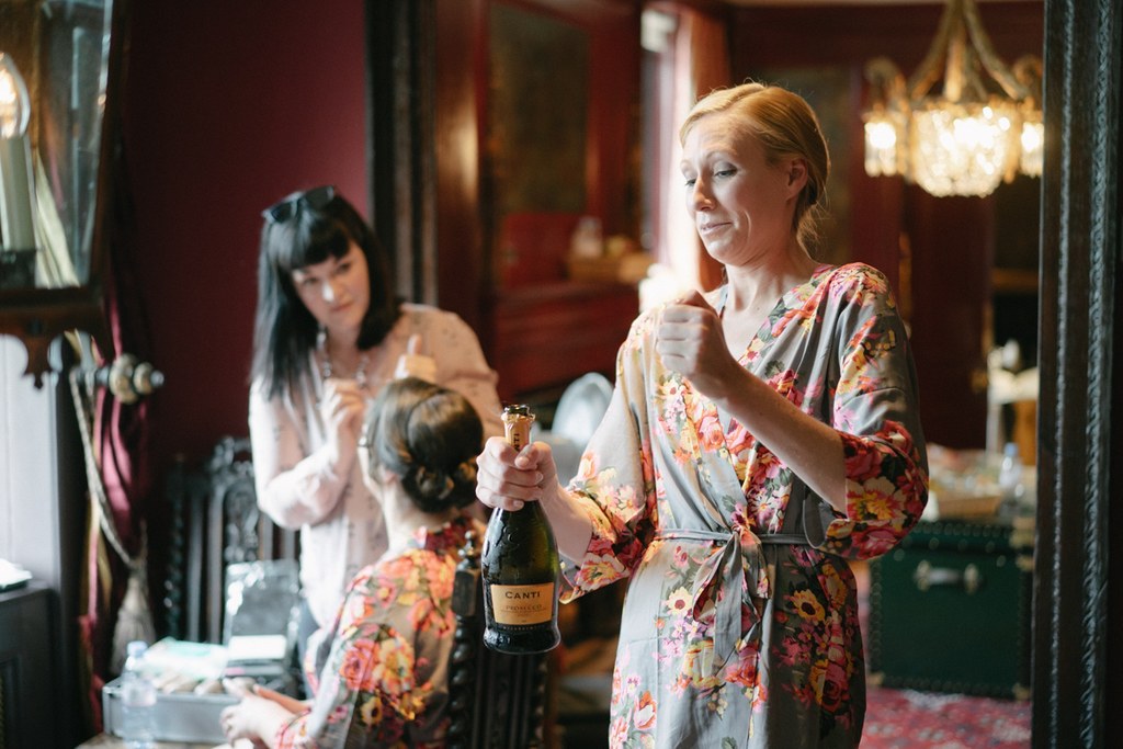 Three women in floral kimonos in a red salon, one holding champagne and Canti bottle, smiling