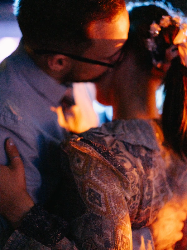 Embracing wedding guest at evening celebration — warm ambient lighting, candid intimate moment, festive atmosphere.
