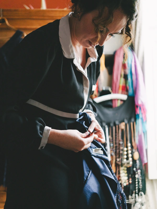 Groom in black suit checks his ring in sunny natural light, colourful ribbons in background