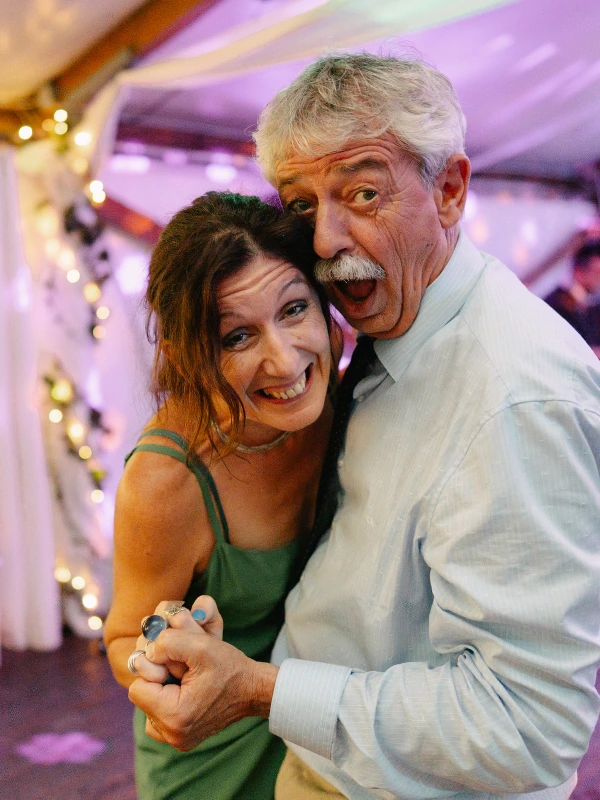 A couple dancing at wedding party — colorful ambient lighting, joyful celebration, festive evening reception moment.