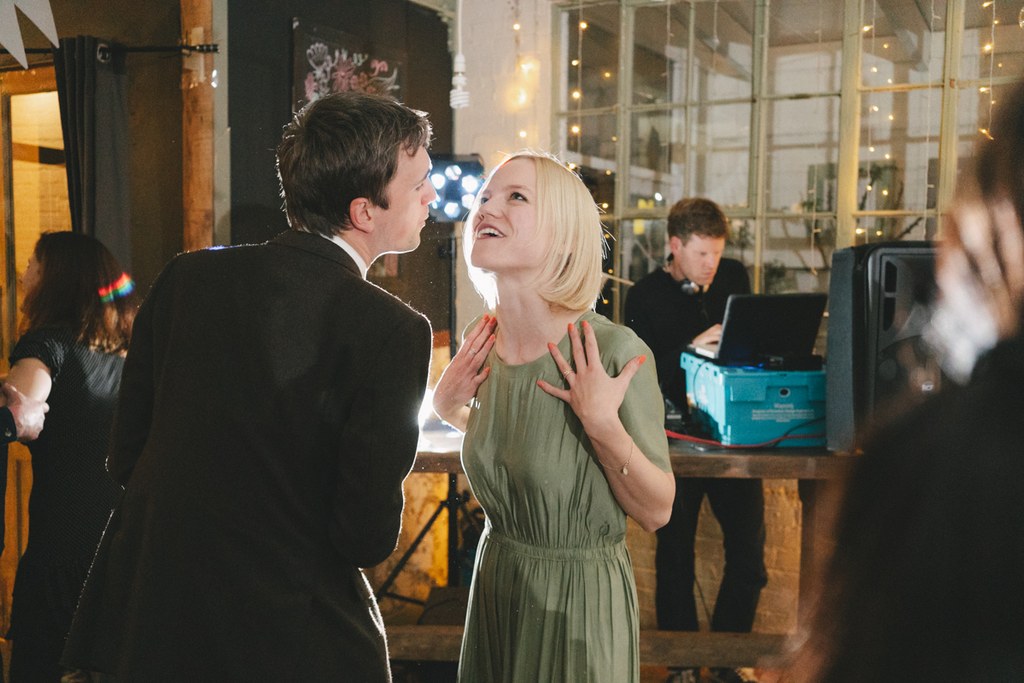 Man and woman dancing at the reception, smiling at each other — warm lighting, glass windows