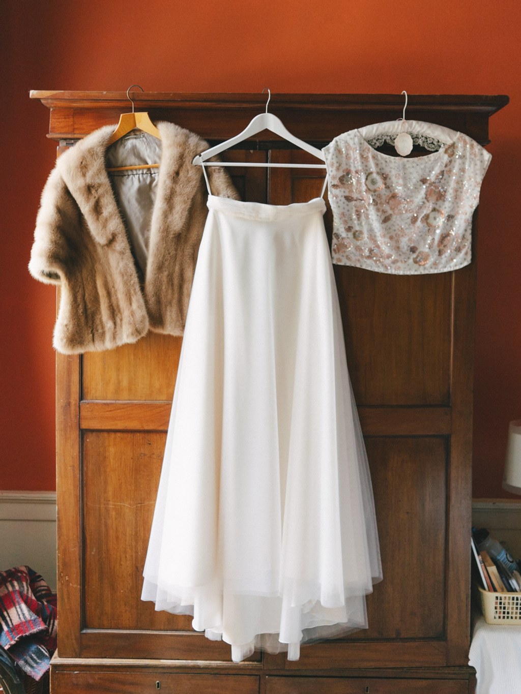 Bridal gown and accessories on an antique wooden wardrobe in front of a terracotta wall