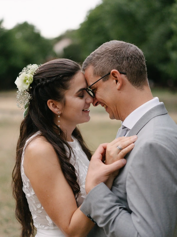 Bride and groom smiling while touching foreheads at outdoor wedding in natural setting.