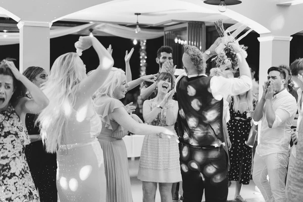 Guests dancing in the marquee — bride with long veil at centre, raised arms, bokeh lights at night