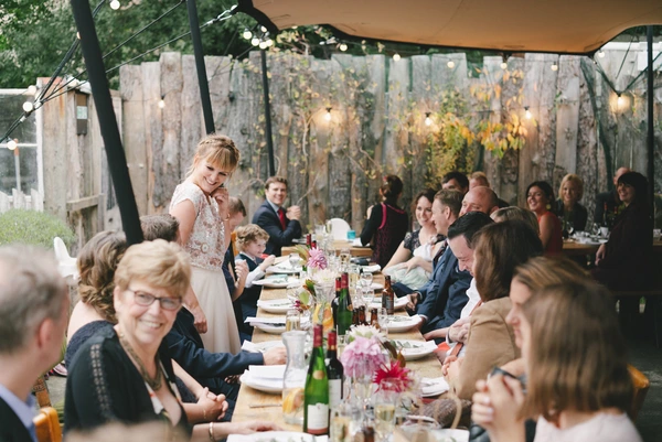 Young bride laughing with guests at the long table under an elegant canopied terrace in autumn