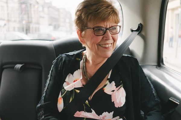 Cheerful female guest in the car, floral dress, sunglasses, radiant smile, cityscape outside