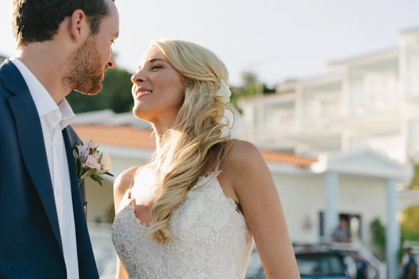 Bride and groom smiling at each other on a sunny terrace — white lace dress, dark blue suit