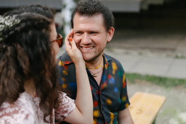 Woman touching man's face playfully during wedding with colorful patterned shirt at outdoor venue.