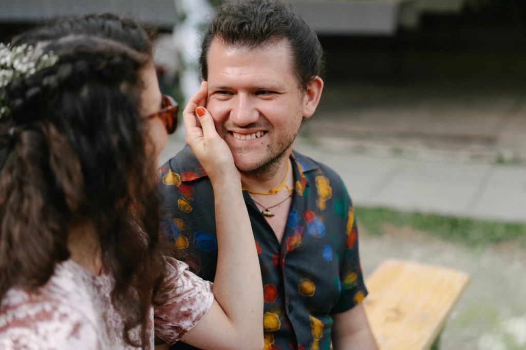 Woman touching man's face playfully during wedding with colorful patterned shirt at outdoor venue.
