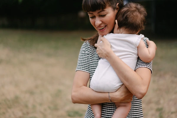 Woman holding and hugging toddler joyfully at outdoor wedding in striped shirt with green background.