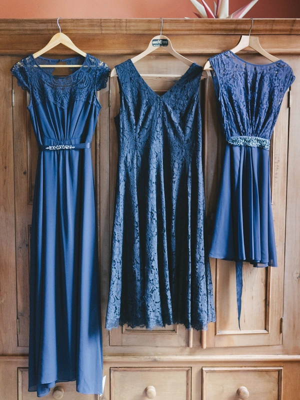 Three blue bridesmaid dresses hanging on a wooden wardrobe — lace, silk and crystal details