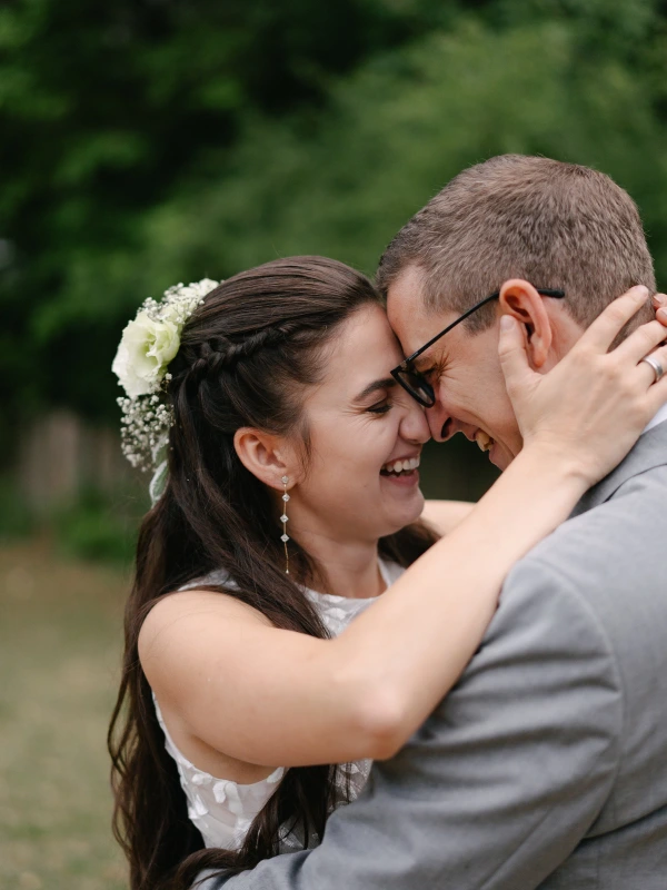 Couple laughing together while hugging at outdoor wedding with intimate moment in natural setting.
