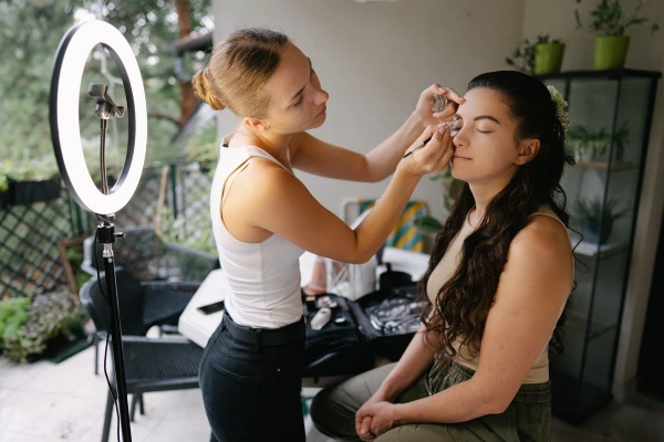 Bride getting her makeup done on a bright terrace using a ring light. Documentary wedding photography.