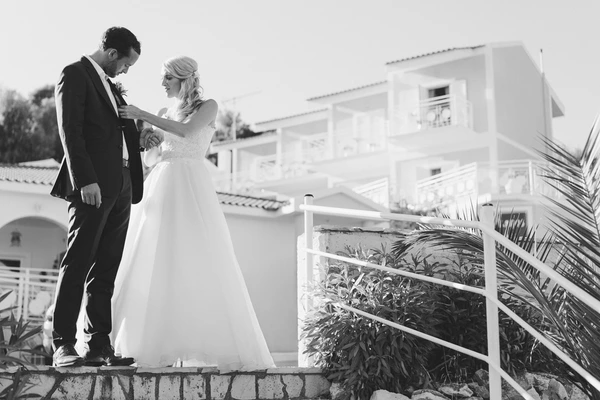 Bride and groom on a terrace — bride smiles, groom looks at her admiringly, white Mediterranean building