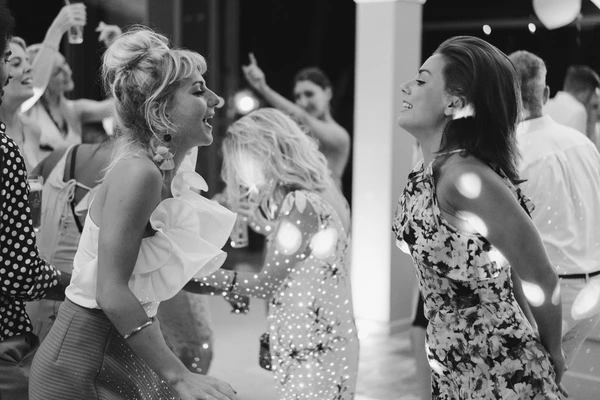 Two women dance and laugh toward each other at the wedding party — guests and decor around them