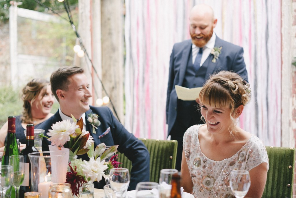 Bride laughing at the speeches at the wedding table, groom and guests with cheerful faces