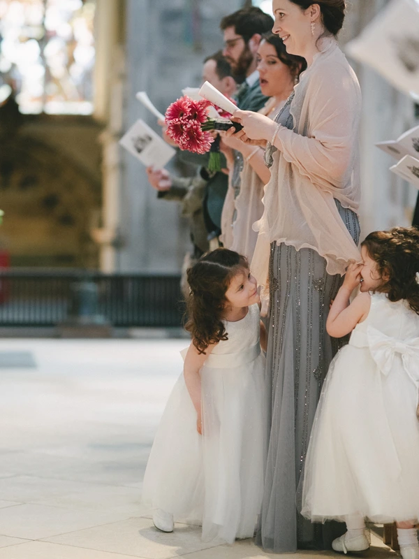 Smiling woman with bouquet and song booklet stands beside two little girls in white tulle dresses