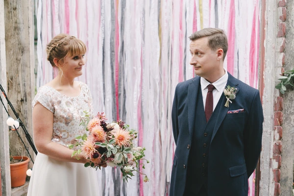Bride and groom looking at each other in front of a colourful ribbon-decorated industrial backdrop