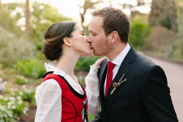 The bride and groom share a close kiss on a garden path surrounded by flowering trees in soft evening light. Romantic documentary wedding portrait at the Royal Botanic Garden Edinburgh.