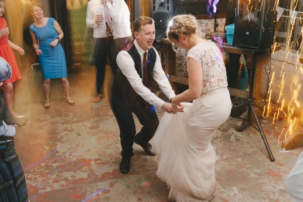 Young couple dances joyfully on the wedding parquet — groom in waistcoat, bride in lace top