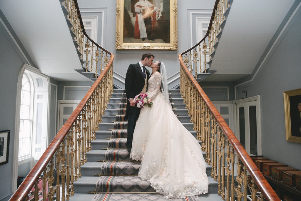 Newlyweds kiss on an elegant staircase — symmetrical gilded railings and painting on the wall