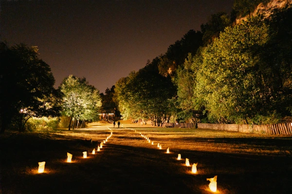 Wedding venue lined with candles at night — garden lights, wooden fence, festive outdoor reception setting.