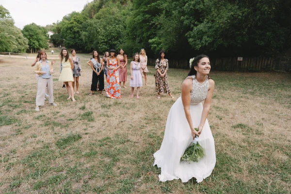 Bride in white dress holding bouquet standing in field with bridesmaids at outdoor wedding ceremony.