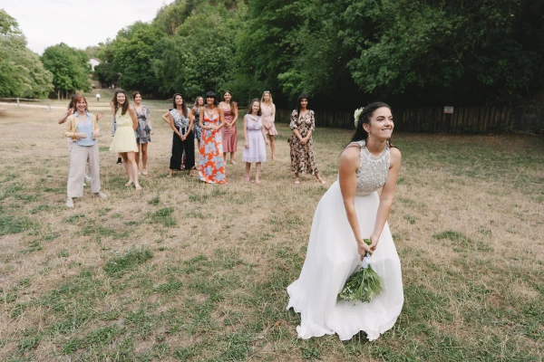 Bride in white dress holding bouquet standing in field with bridesmaids at outdoor wedding ceremony.