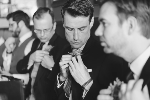Groom concentratedly ties his cravat with the best man's help before the ceremony — black-and-white