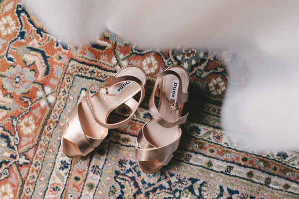 Elegant nude-gold wedding shoes on a patterned rug in natural light