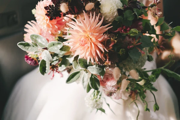 Bridal bouquet detail — peach dahlias, white roses, dark red flowers and green eucalyptus