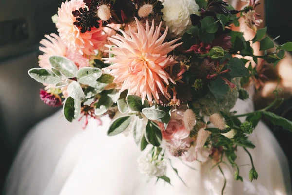 Bridal bouquet detail — peach dahlias, white roses, dark red flowers and green eucalyptus