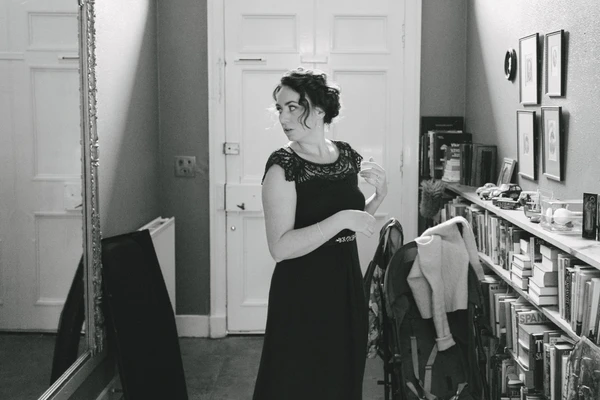 Bride in black lace dress before the mirror, hair up, holding white fabric — getting ready