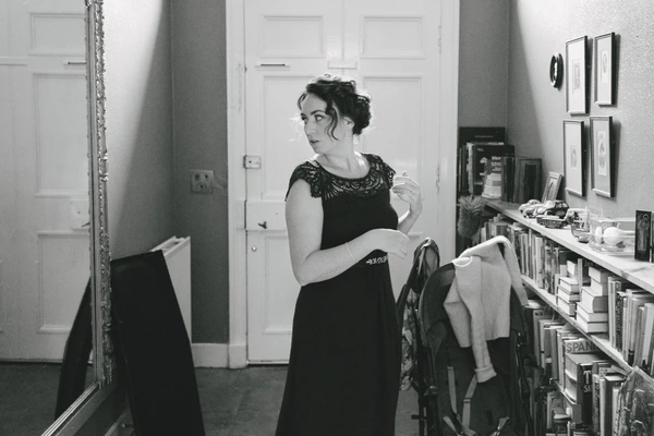 Bride in black lace dress before the mirror, hair up, holding white fabric — getting ready