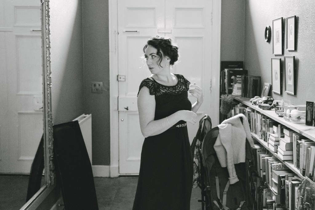 Bride in black lace dress before the mirror, hair up, holding white fabric — getting ready