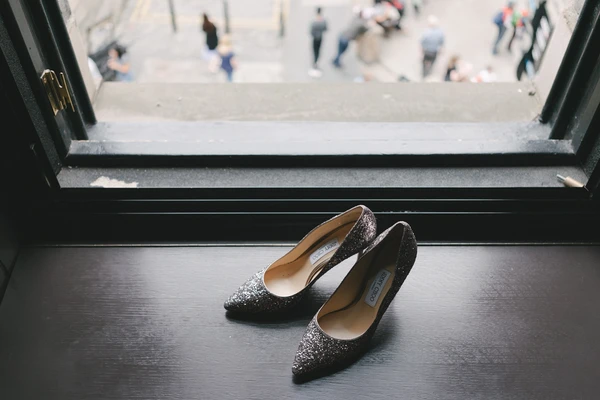 Black sparkling bridal shoes on a window ledge, blurred town square and wedding guests behind