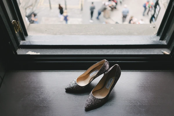 Black sparkling bridal shoes on a window ledge, blurred town square and wedding guests behind