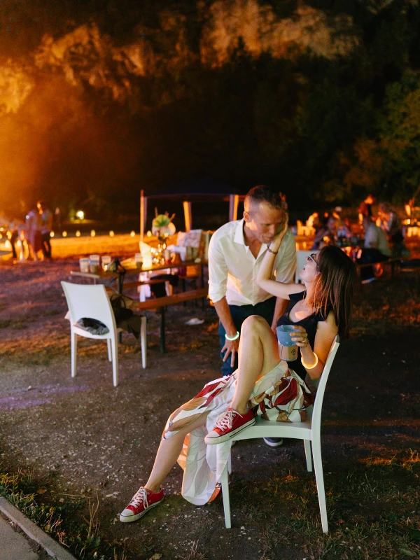 Couple chatting at outdoor evening wedding celebration — warm golden stage lighting, intimate conversation, garden venue.