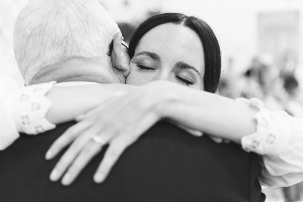 Black and white close-up of the bride pressing her cheek against an older man's cheek in a tender embrace at the wedding reception. Candid documentary wedding photography.