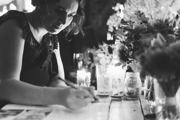 Woman examining refreshment glasses at a decorative table surrounded by flowers and natural light