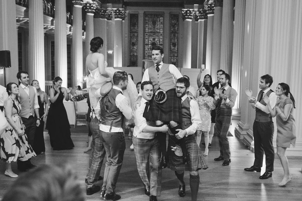 Bride and groom perform a lift amid guests in an elegant columned hall during the wedding dance
