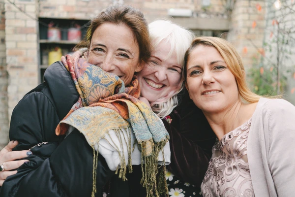 Three women in a close embrace laughing, a baby with a colourful scarf in the centre